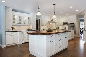 Bespoke white kitchen cabinets, brown wooden floor and white walls.